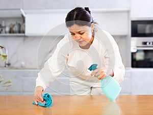 Positive young woman cleaning kitchen table at home