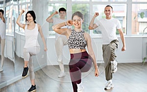 Positive young woman dancing modern dance with other people during group training