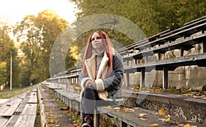 Positive young woman with dreadlocks looking away, smiling, sitting on old shabby bench of street bleacher in golden