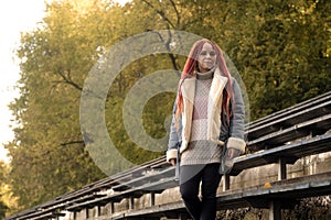 Positive young woman with dreadlocks looking at camera, smiling, posing near old shabby bench of street bleacher in