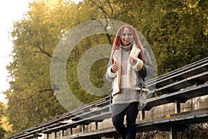 Positive young woman with dreadlocks looking at camera, smiling, posing near old shabby bench of street bleacher in