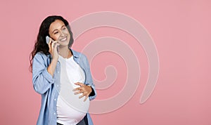 Positive young woman expectant talking on phone, pink background