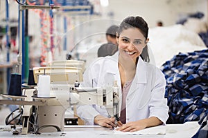 Positive young woman sewing with professional machine at workshop