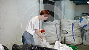 Positive young woman worker in latex gloves sorting glass and plastic garbage at modern light waste recycling plant