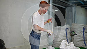 Positive young woman worker in latex gloves sorting glass and plastic garbage at modern light waste recycling plant