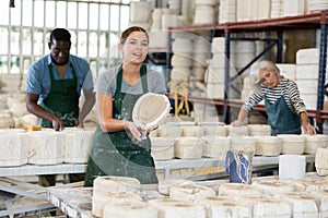 Positive young worker demonstrates half of plaster mold for pottery in pottery factory