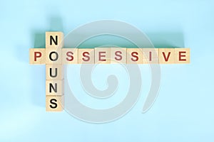 Possessive Nouns concept in English grammar education. Wooden block crossword puzzle flat lay in blue background. photo