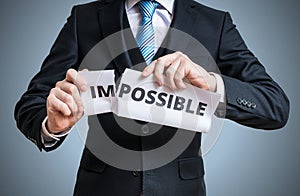 Possibility concept. Man is tearing paper with impossible word