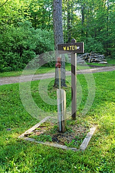 Water spigot on grassy campground with wood sign