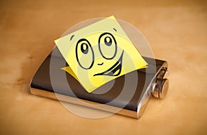 Post-it note with smiley face sticked on hip flask