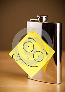 Post-it note with smiley face sticked on a hip flask