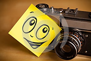 Post-it note with smiley face sticked on photo camera