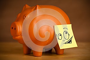 Post-it note with smiley face sticked on a piggy bank