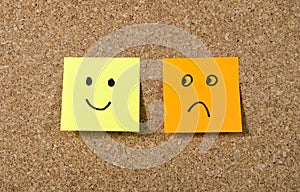 Post it notes on corkboard with smiley and sad cartoon face expression in happiness versus depression concept