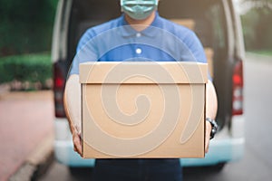 Postal delivery courier man wearing protective face mask in back of cargo van delivering package holding box due to Coronavirus