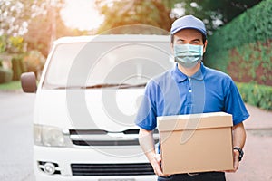 Postal delivery courier man wearing protective face mask in front of cargo van delivering package holding box due to Coronavirus