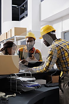 Postal workers checking parcel invoice on laptop and clipboard