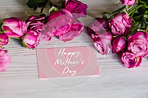 Postcard with bouquet of small pink roses on white rustic wooden background. Happy mother`s day text sign. Greeting card with