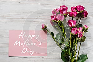 Postcard with bouquet of small pink roses on white rustic wooden background. Happy mothers day text sign. Greeting card