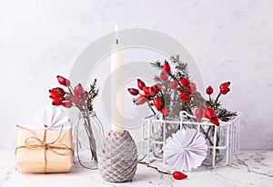 Postcard with  burning candle, wrapped box with present, briar berries in bottle, against textured  wall.