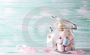 Postcard with glass jar full of colorful sweet marshmallows with emty tag on turquoise wooden background.