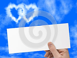 Postcard in hand, blue sky and heart-shaped clouds