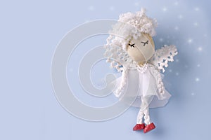 Postcard layout with a cute handmade angel in white clothes on a light blue background with bokeh. Copy space