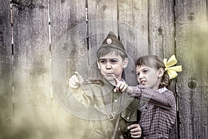 Postcard, stylized as vintage for the Victory Day. A boy in a military uniform and a girl in an old dress are standing near an old