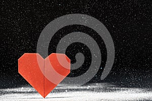 Postcard for Valentinan Day. A red heart on a black background, sparkles falling, snow, a place for text.