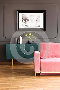 Poster above green cupboard in grey loft interior with pink couch on wooden floor