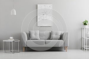 Poster above grey couch in minimal living room interior with lamp above table. Real photo