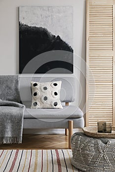 Poster above grey settee with patterned cushion in natural living room interior. Real photo