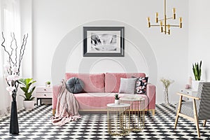 Poster above pink sofa in spacious living room interior with patterned armchair and plants. Real photo