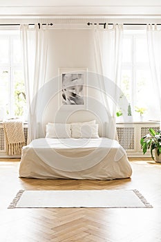 Poster above white bed in minimal bedroom interior with drapes a