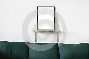 Poster in black frame in white stylish modern interior on a wall above green sofa. Design template mockup.