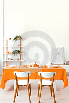 Poster on cabinet in white and orange dining room interior with wooden chairs at table