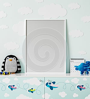 Poster frame mock up in children`s room with light blue wall with clouds, chest of drawers with planes print, penguin soft toy,