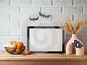Poster frame mock up for Halloween holiday. Wheat in modern vase and pumpkin decoration on wooden table over brick wall background