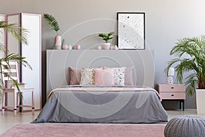 Poster on grey bedhead in bedroom interior with pink pillows on photo