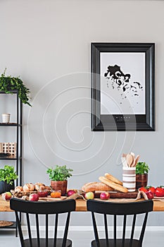 Poster on grey wall in dining room interior with black chairs at wooden table with food