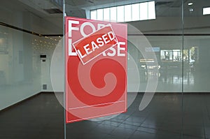 Poster of `For Lease` with a `Leased` sign on top in front of a vacant shop. Concept of rental commercial property