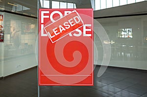 Poster of `For Lease` with a `Leased` sign on top in front of a vacant shop. Concept of rental commercial property or retail s photo