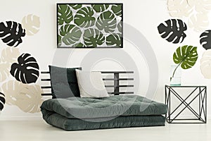 Poster of leaves above futon with cushions in modern bedroom int