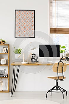 Poster on white wall above wooden desk with lamp and desktop com