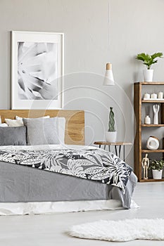 Poster on wooden headboard of bed with grey sheets in bright bed