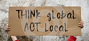 A poster with the words THINK GLOBAL ACT LOCAL in the hands of a young girl against a textured wall