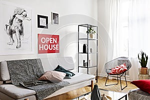 Posters above sofa with pillows and blanket in bright living room interior with armchair. Real photo