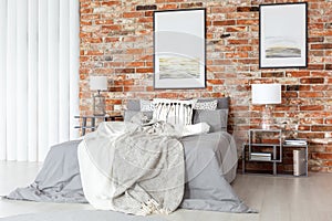 Posters on a bare, red brick wall, above a cozy bed with gray sh