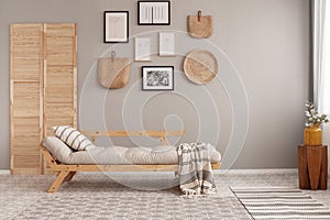 Posters in black frames and wicker kinck knack on beige wall of trendy living room interior with long settee with