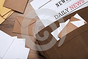 Postman bag, newspapers and mails on wooden table, flat lay